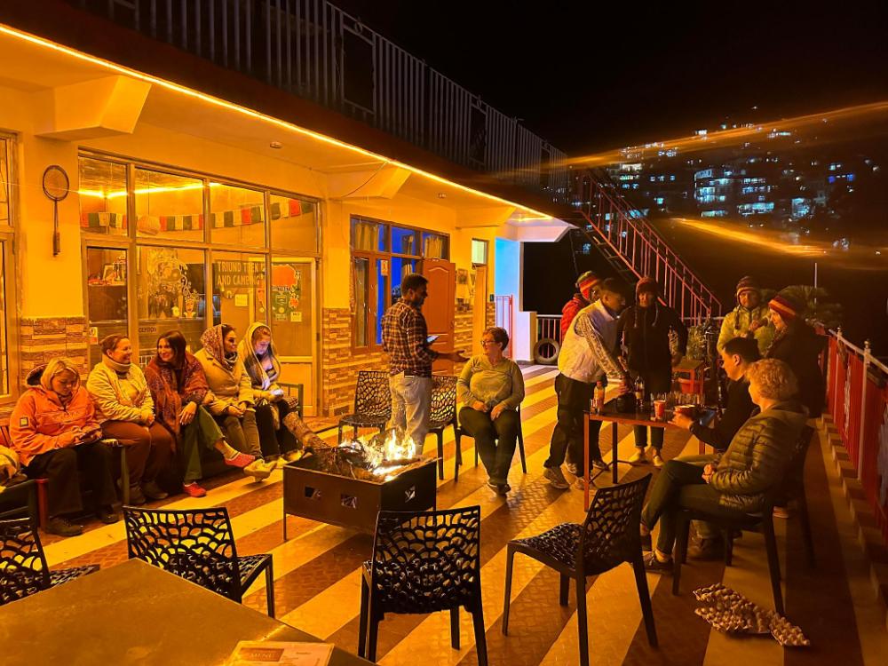 The rooftop bar at night, warm amber lights and guests around the bonfire