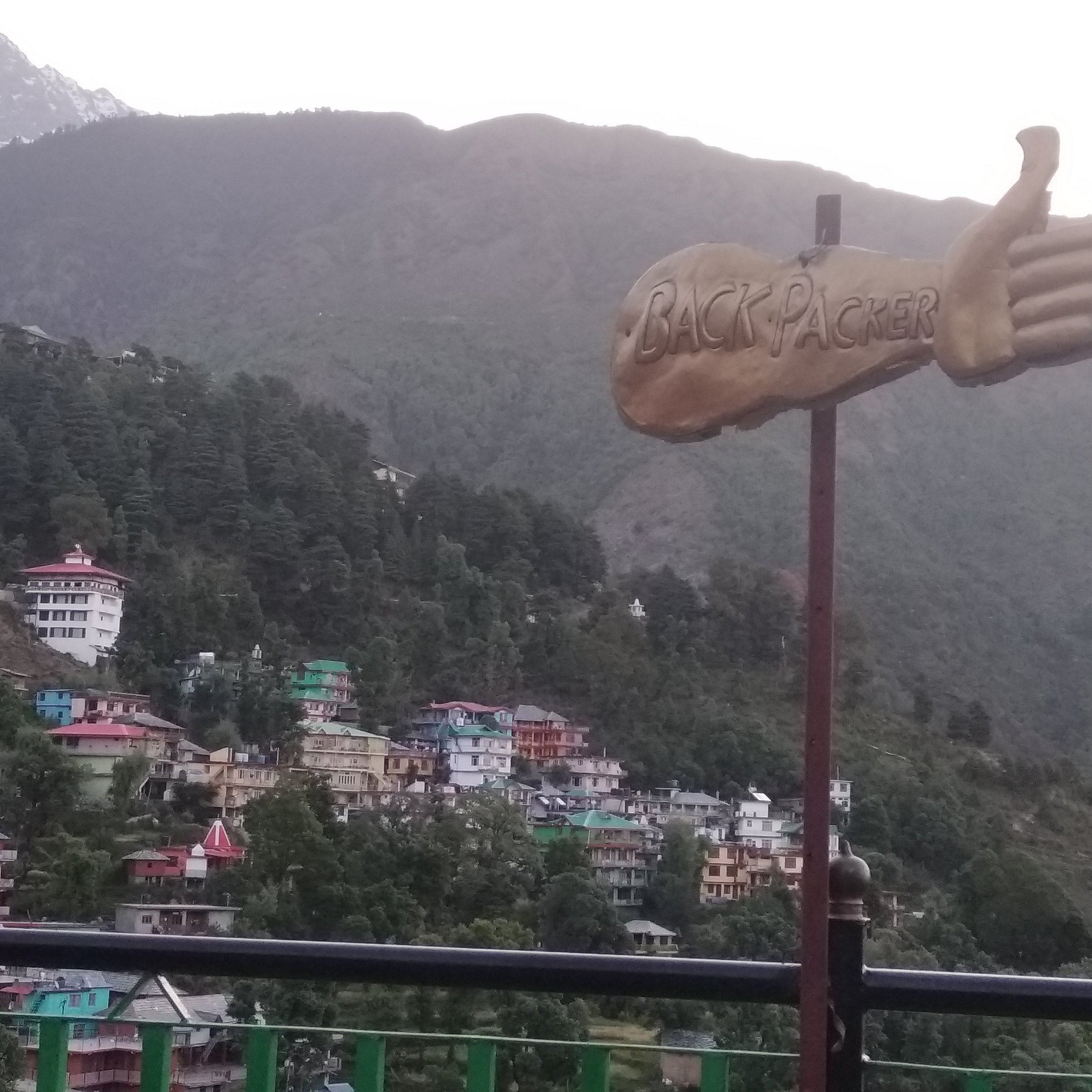 The Backpackers Inn thumb logo sign pointing at the colourful McLeod Ganj hillside